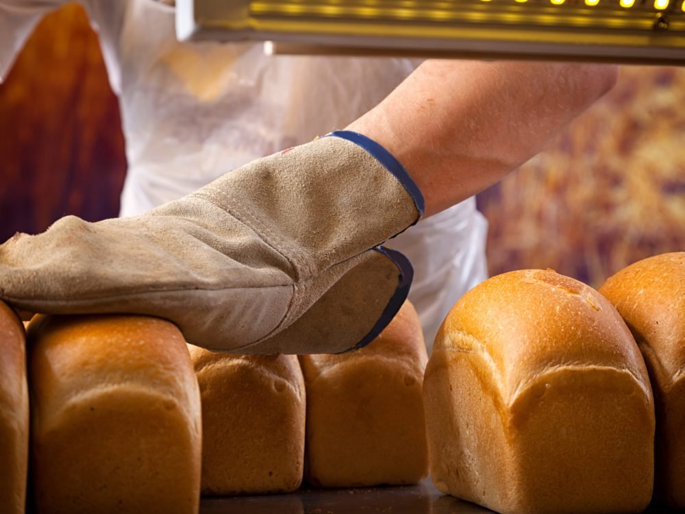 A close-up of a baker's man in a protective glove touches a freshly baked fresh bread, which he just took out of the oven